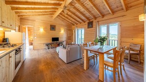 A wooden cabin interior with a dining area, sofa, TV, and kitchen.