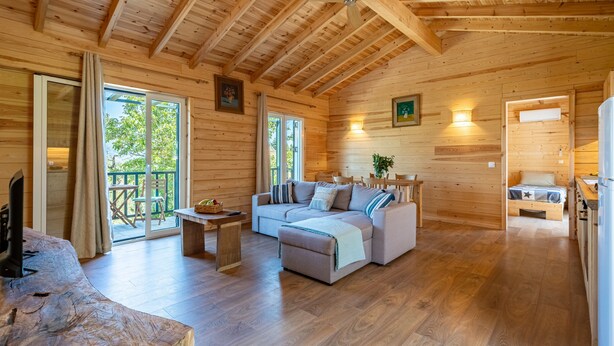 A wooden cabin interior with a sofa, dining table, and a kitchen area.