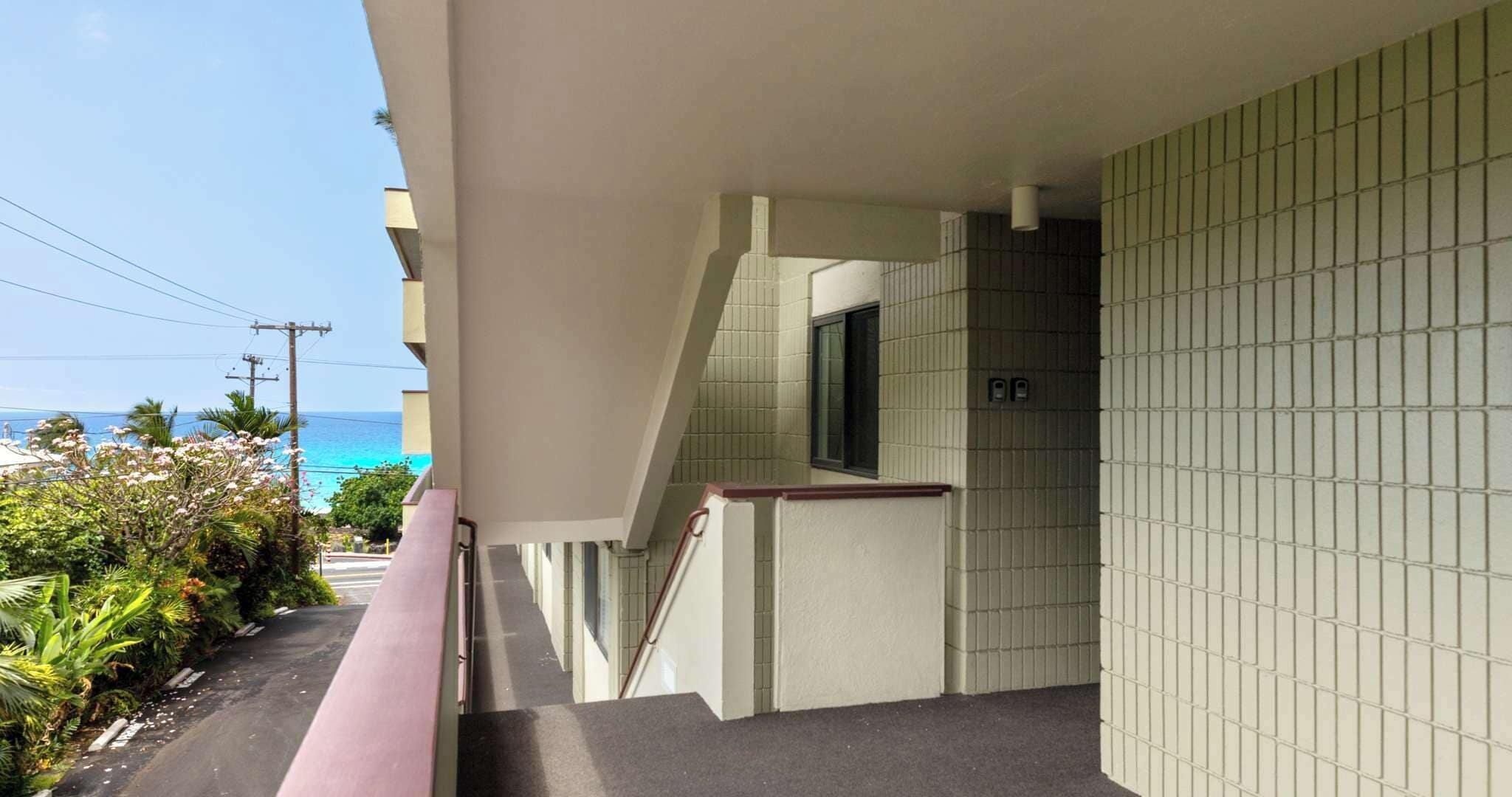 A balcony with a view of the ocean, a tiled wall, and a staircase leading to an upper floor.