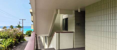 A balcony with a view of the ocean, a tiled wall, and a staircase leading to an upper floor.