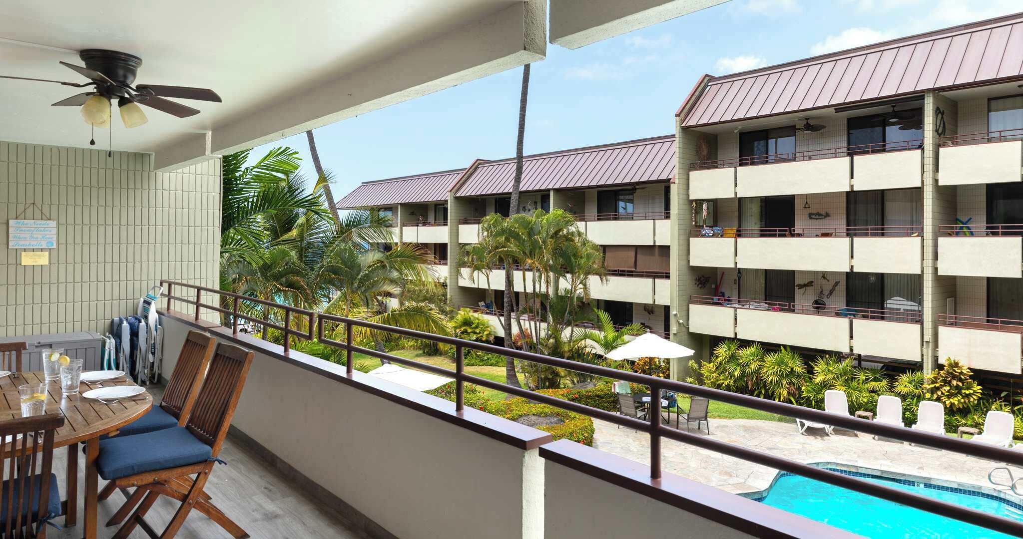 A balcony with a pool, wooden furniture, and a view of a multi-story building with balconies.