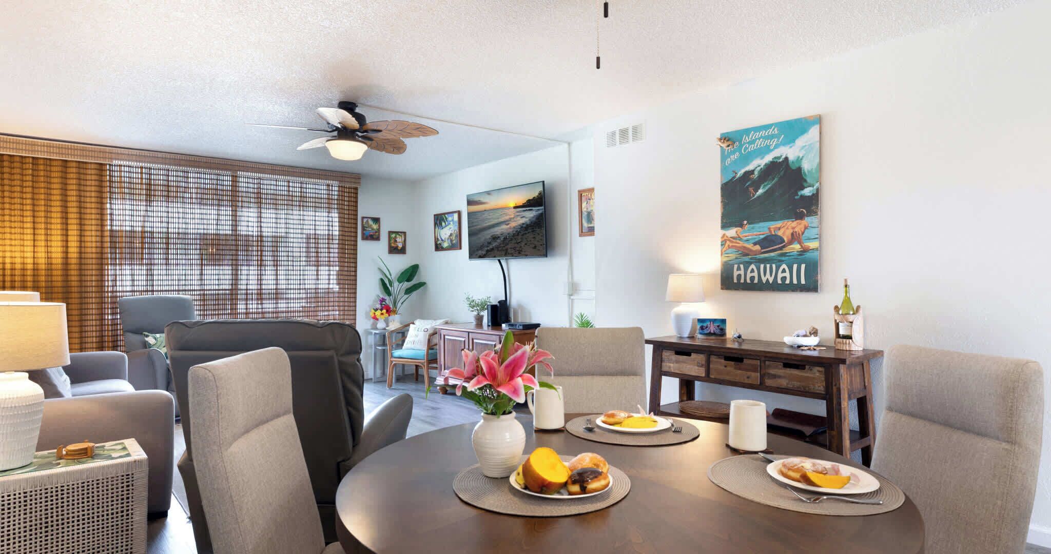 A modern living room with a round dining table, grey sofas, and a ceiling fan.