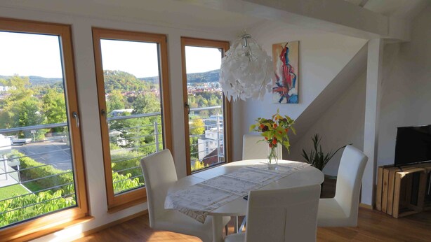 A dining area with a table, chairs, a vase with flowers, a painting, and a TV on a wooden cabinet. - Apartment 'Loft Straussi' with Shared Garden and Wi-Fi (Tuttlingen)