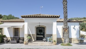 A building with a tiled roof, a stone archway entrance, outdoor seating, and a palm tree. - Apartment 'Arroyuelo' with Mountain Views, Wi-Fi and Air Conditioning (Prado del Rey)