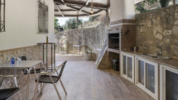 A covered outdoor dining area with a stone wall, a grill, and a table with chairs. - Apartment 'Arroyuelo' with Mountain Views, Wi-Fi and Air Conditioning (Prado del Rey)