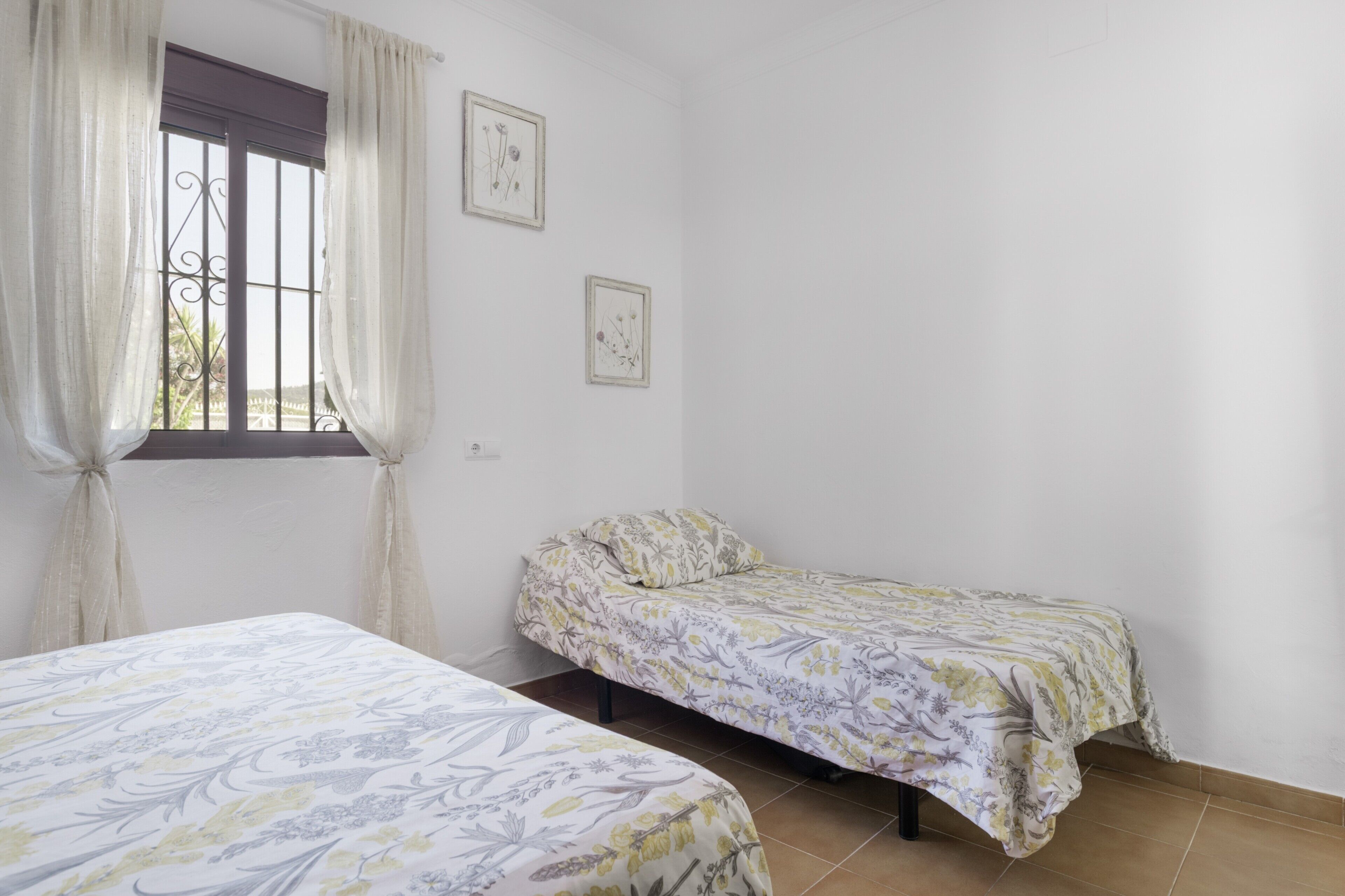 Una habitación con dos camas, una ventana con cortinas y dos cuadros en la pared.