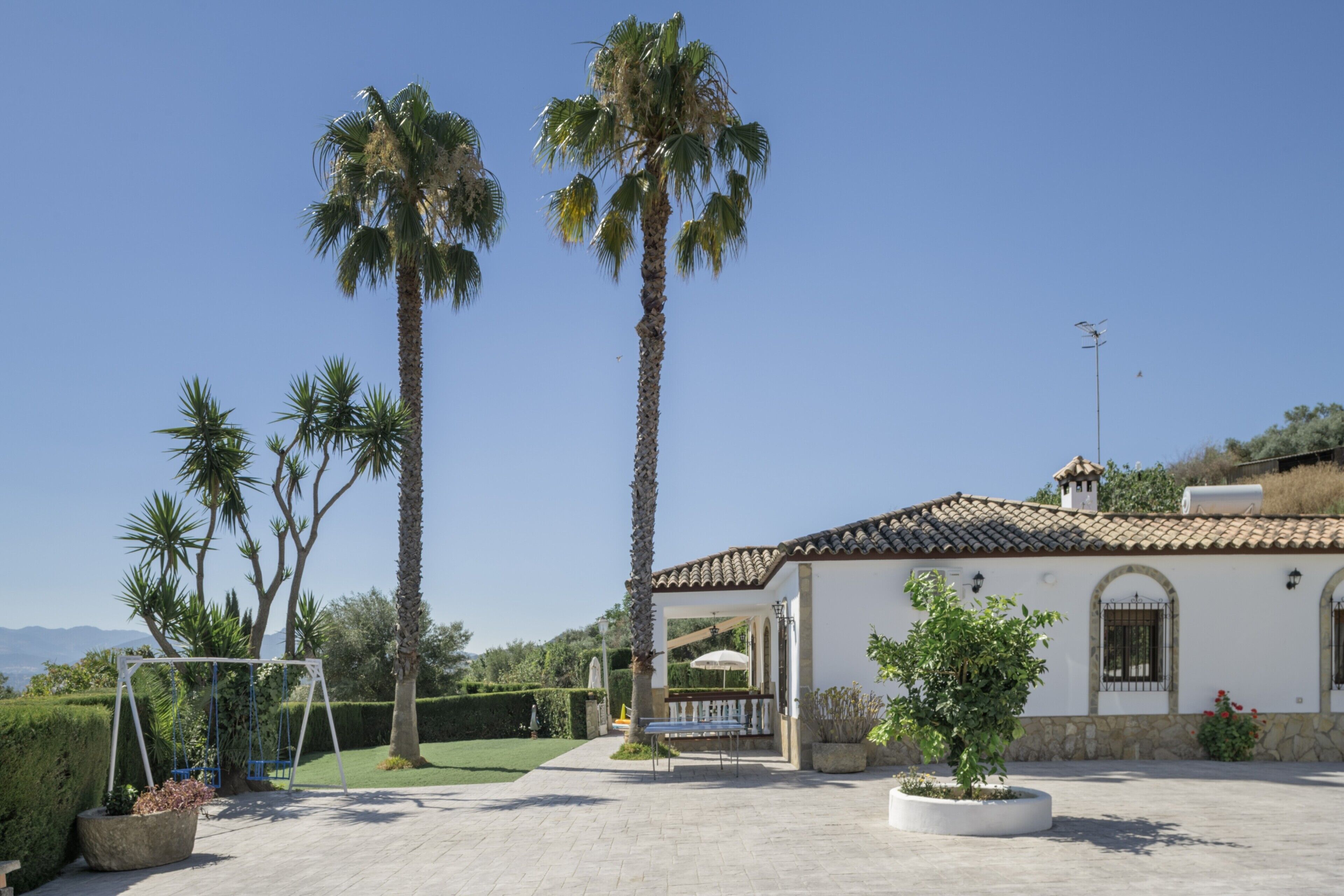 Un edificio blanco con techo de tejas, un patio con un columpio y palmeras.