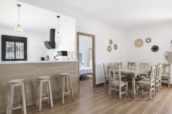 A modern kitchen with wooden stools, a dining table with chairs, and a large window.