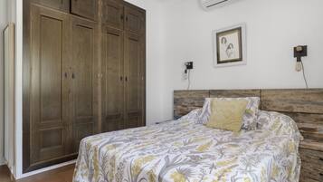 Een slaapkamer met een bed, een houten garderobe, een wandairconditioner en een lijst met een afbeelding.