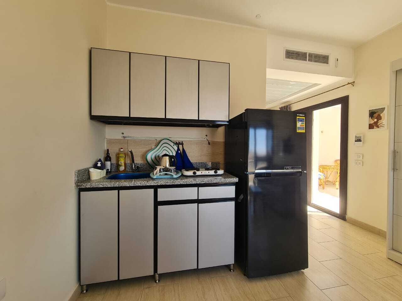 Cocina compacta con un refrigerador negro, un microondas y un lavamanos. Hay armarios sobre la encimera y un sistema de ventilación en la pared.