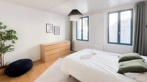 A bedroom with a bed, a dresser, a plant, and a window.