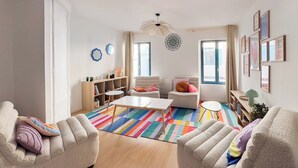 A living room with a white sofa, a coffee table, a bookshelf, and a colorful striped rug.