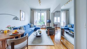 A modern living room with a blue sofa, a dining table with breakfast, and a TV on a stand. - Sunny European Studio Mas A-41 (Brussels)