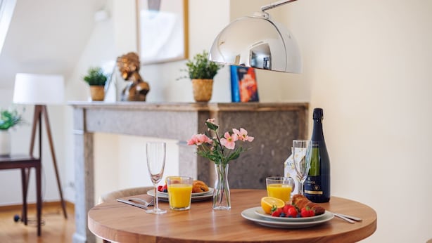Une table ronde en bois, sur laquelle sont disposés des aliments pour le petit-déjeuner, notamment des croissants, des fruits, du jus et une bouteille de vin.