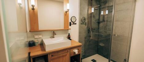 A modern bathroom with a wooden vanity, a large mirror, and a glass-enclosed shower.