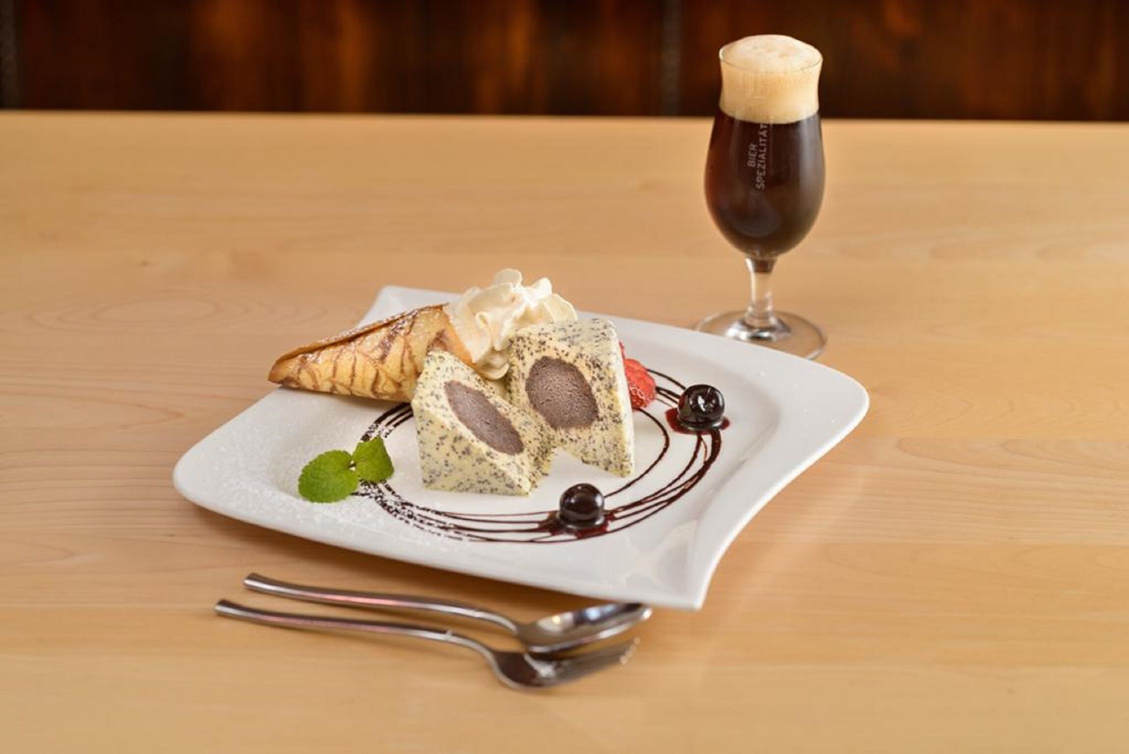 A dessert plate with a pastry and a glass of dark beer on a wooden table.