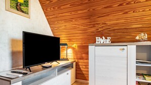 A modern room with a flat-screen TV on a wooden console, a small cabinet with a 'HOME' sign, and a bookshelf with books. - Holiday Appartment "Anne" with Balcony and Wi-Fi (Bremervörde)