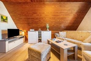 A cozy living room with a wooden ceiling, a flat-screen TV, a sofa, a coffee table, and a small cabinet.