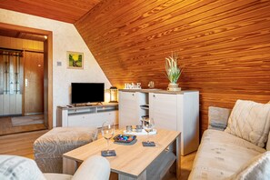 A cozy room with a wooden ceiling, a TV, a dining table with glasses and a bowl, and a sofa.