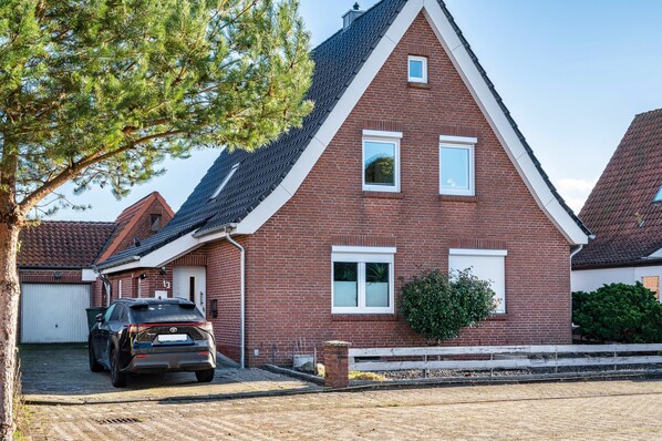 A red brick house with a car parked in the driveway, a small window, and a tree in the foreground.
