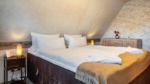 A bedroom with a large bed, bedside lamps, a wooden nightstand, a brick wall, and a small table with a vase. - Holiday Appartment "Anne" with Balcony and Wi-Fi (Bremervörde)