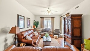 A living room with a brown leather sofa, a glass coffee table, a wooden cabinet, and a ceiling fan. - Kings Grant 203- 2BR Ocean Drive- Pool, Hot Tub (North Myrtle Beach)