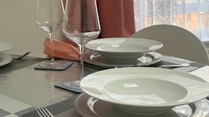Une table à manger dressée avec des assiettes, des couverts et des verres à vin, agrémentée d’un chemin de table à motifs et d’une serviette.