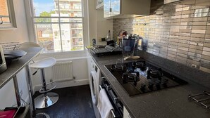 Une cuisine moderne dotée d’une cuisinière intégrée, d’une fenêtre offrant une vue sur les immeubles et d’un pare-feu en carreaux.