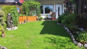Ein gepflegter Garten mit Rasen, Holzzaun und verschiedenen Blumentöpfen.