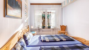 Ein Schlafzimmer mit Bett, Stuhl, einem Fenster mit Vorhängen und einem Bild an der Wand.