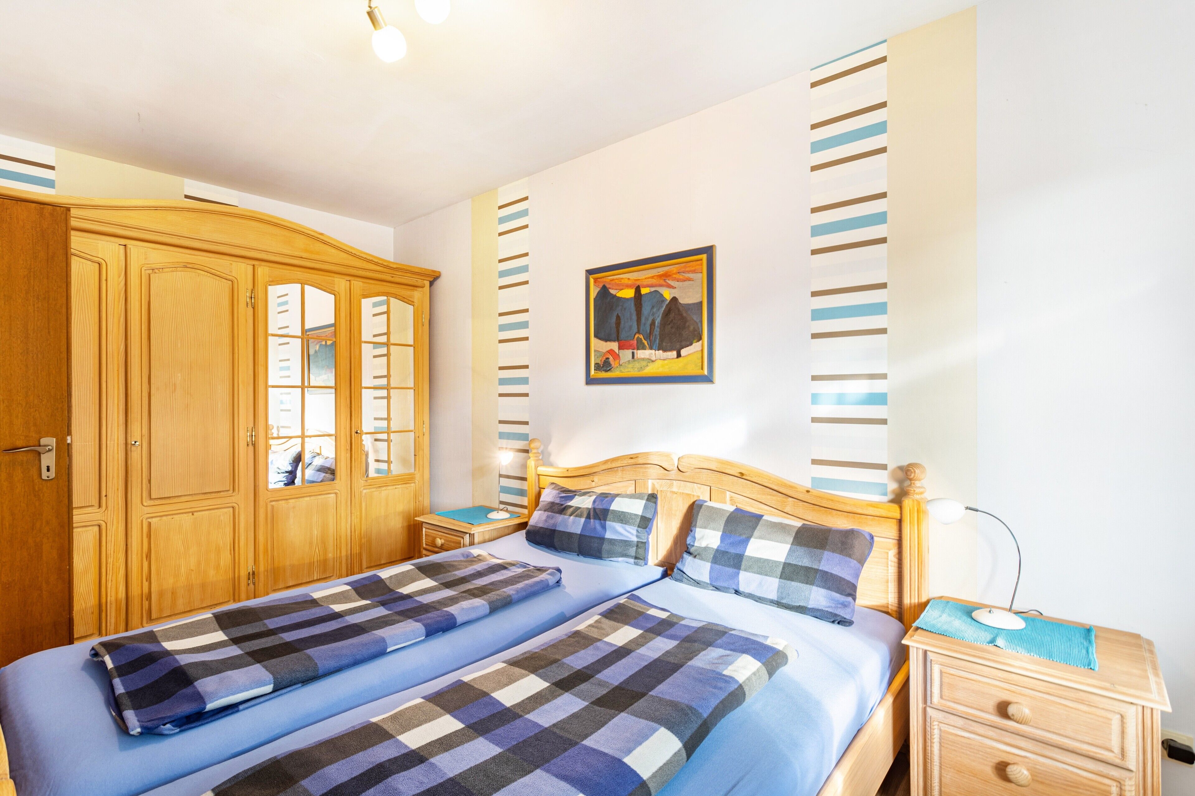 Een slaapkamer met een tweepersoonsbed, een houten garderobe, nachtkastjes en een schilderij aan de muur.