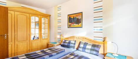 Een slaapkamer met een tweepersoonsbed, een houten garderobe, nachtkastjes en een schilderij aan de muur.
