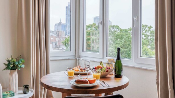 A breakfast table with a bottle of champagne, a bowl of fruit, and orange juice. - Suite Mas B-42 Studio - Split Level (Brussels)