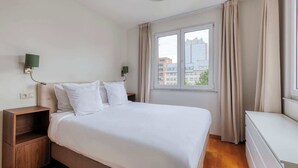 A hotel room with a large bed, two bedside tables, a nightstand, a window with curtains, and a view of buildings outside. - Suite Mas B-42 Studio - Split Level (Brussels)