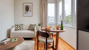 A small, modern room with a sofa, a dining table with breakfast, and a large window with a city view. - Suite Mas B-42 Studio - Split Level (Brussels)