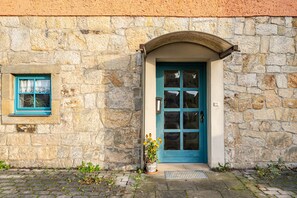 A stone building with a blue door and window, a potted plant, and a metal grate at the entrance. - Holiday Home 'Gemütliches In Lohmen' with Seating Area in Front of the Apartment and Wi-Fi (Lohmen)