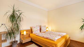Un dormitorio con cama, lámparas de noche, mesita de noche, planta en maceta y cabecero de madera.
