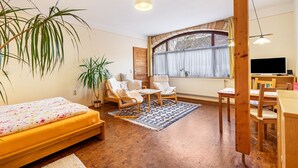 Une pièce confortable avec un lit, deux fauteuils, une petite table, un téléviseur et une fenêtre avec des rideaux.