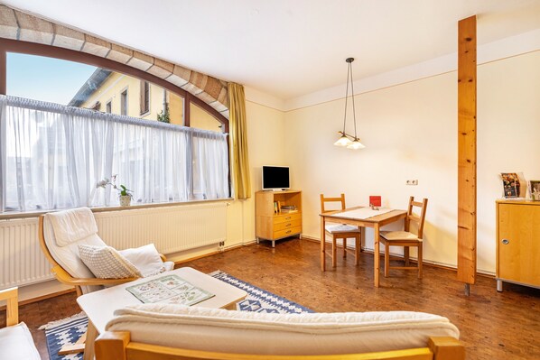 A cozy room with a bed, a desk, a chair, a television, and a window with curtains.