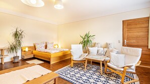 Une chambre à coucher moderne avec un lit, deux chaises blanches, une table en bois, un tapis à motifs et deux plantes en pot.