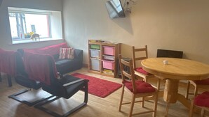 A room with a black sofa, a red rug, a wooden table, and a TV mounted on the wall.