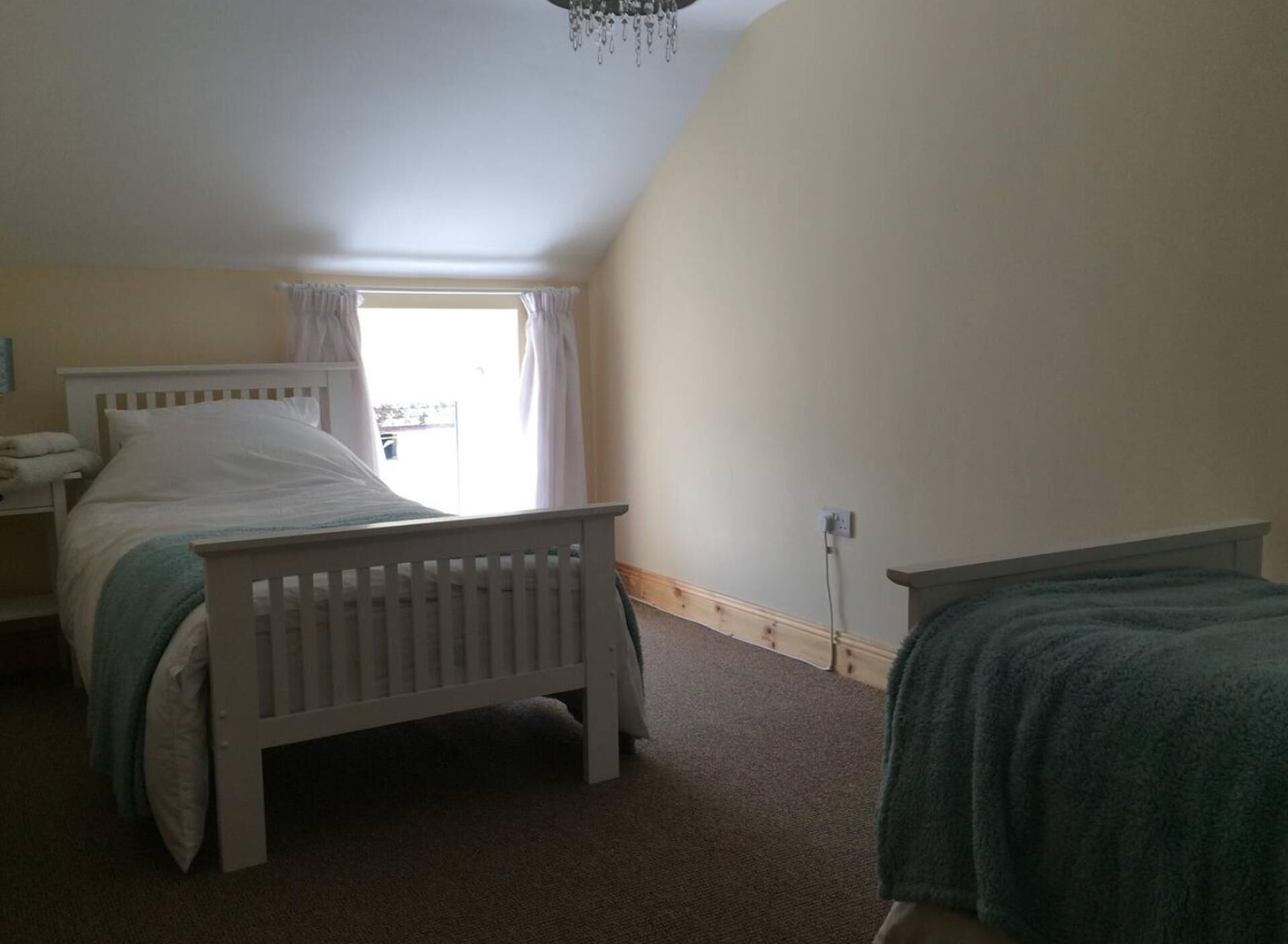 Une chambre avec un lit simple, une table de chevet, une fenêtre avec des rideaux et un sol recouvert d’une moquette.