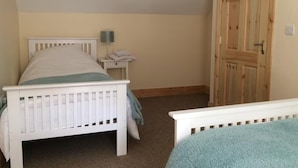 A bedroom with a single bed, a nightstand, a lamp, and a wooden door.