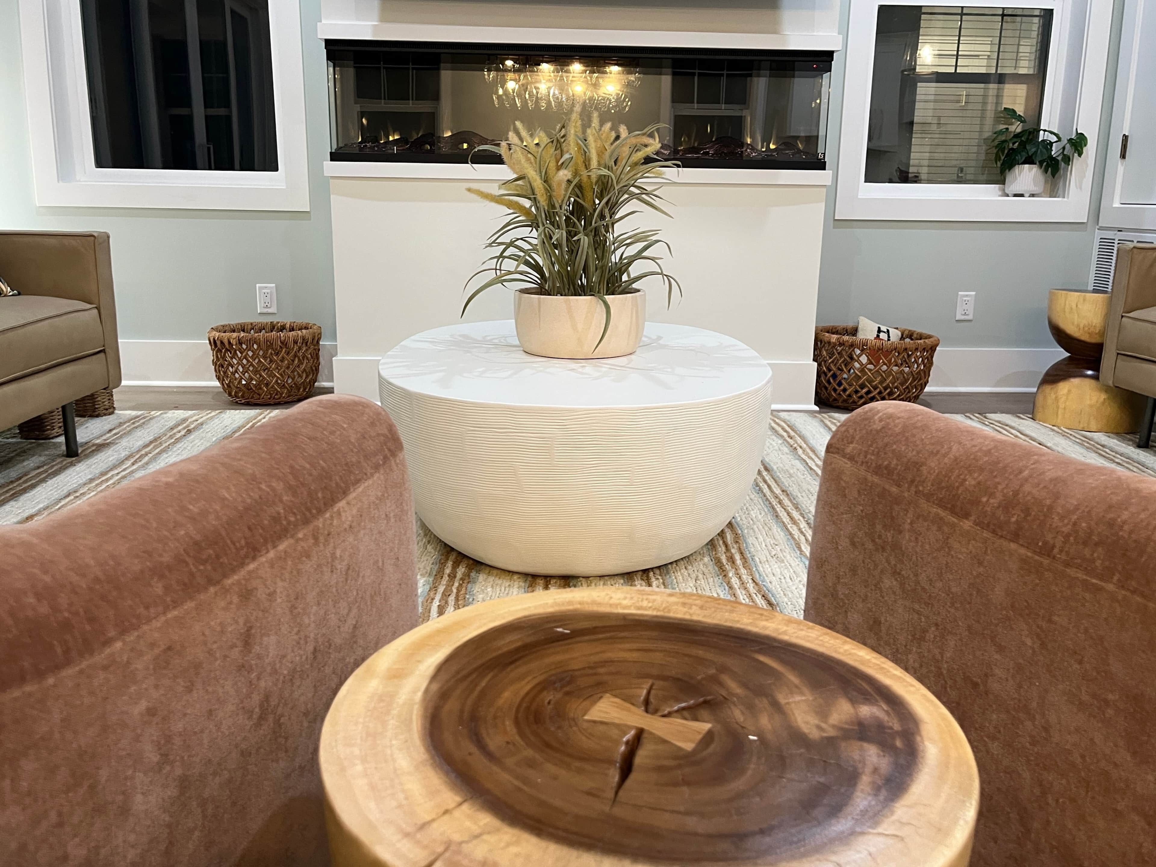 A modern living room with a round coffee table, two sofas, a fireplace, and a view of the outdoors.