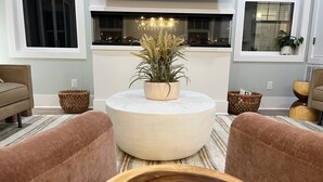 A modern living room with a round coffee table, two sofas, a fireplace, and a view of the outdoors.