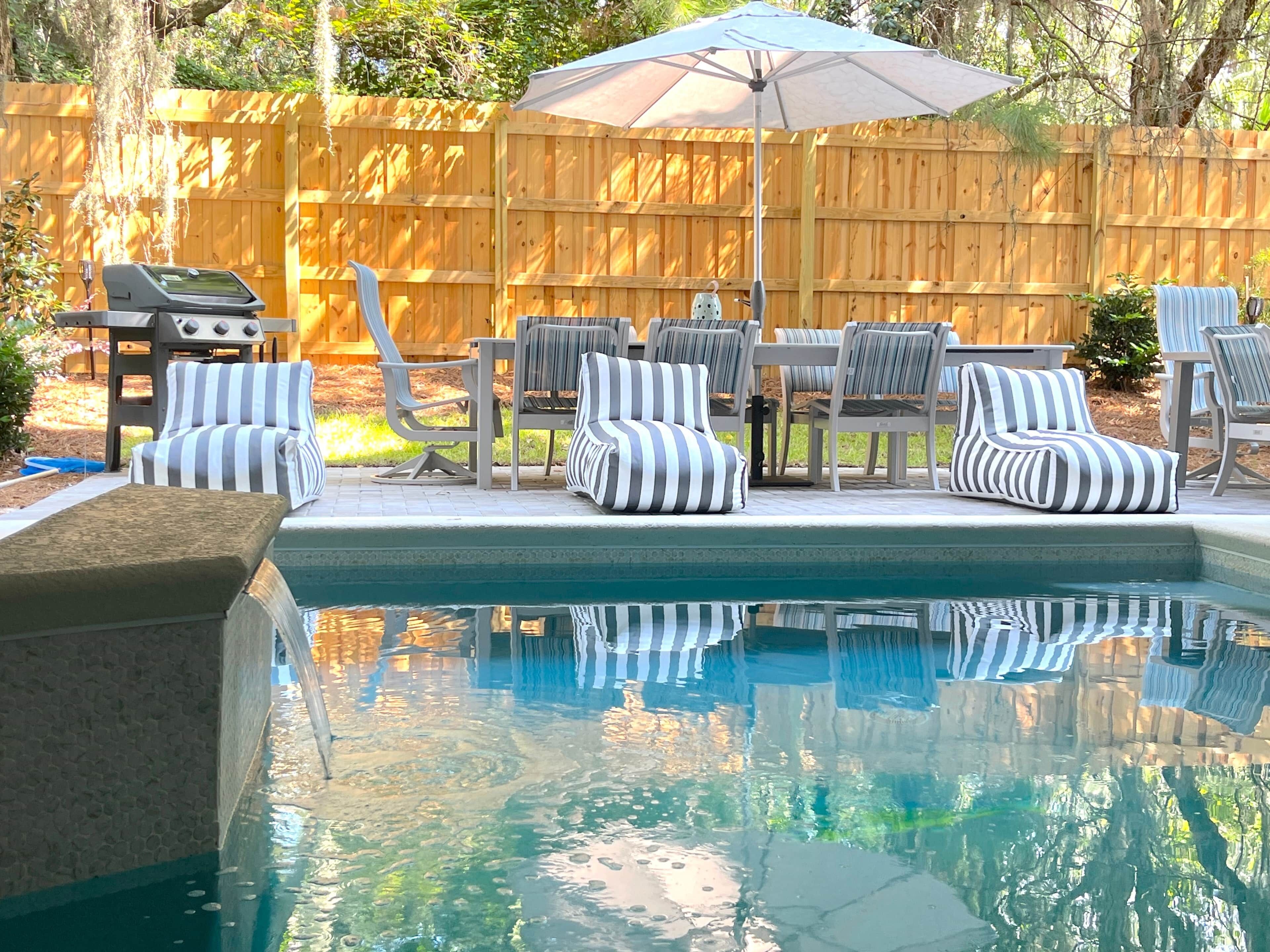 A swimming pool with a wooden fence, outdoor furniture, and a grill.