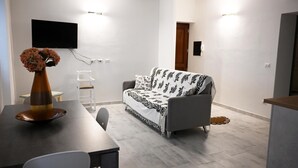 A modern living room with a sofa, a dining table with chairs, a vase with flowers, and a flat-screen TV mounted on the wall. - Apartment Rena Bianca IUN S4020 (Santa Teresa Gallura)