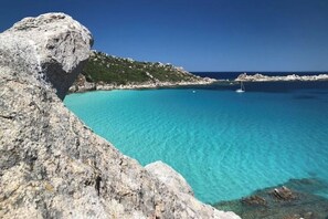 A coastal landscape with clear turquoise waters, rocky formations, and a sailboat.
