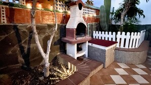 Un patio al aire libre con un horno de piedra, una valla de piquetes blancos y un cactus.