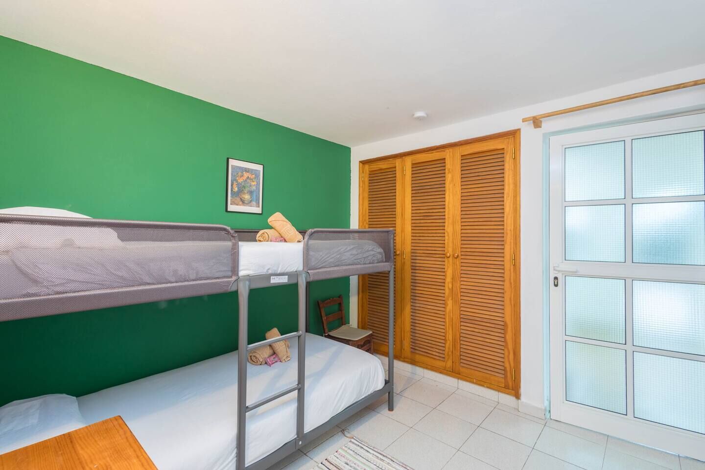A room with bunk beds, a green wall, a wooden door, and a window with blinds.